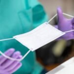 Hands in protective gloves holding protective mask