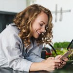 smiling-young-woman-using-smartphone-in-kitchen-3K5MASW.jpg